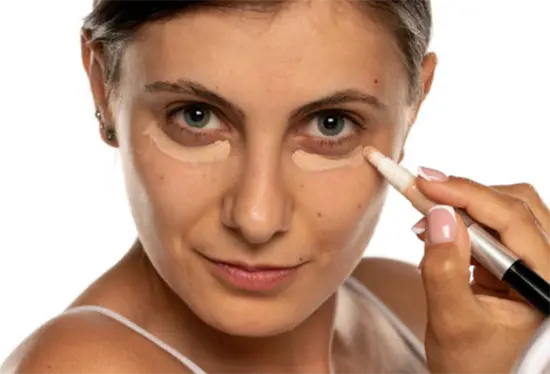 A woman applying concealer under her left eyelid