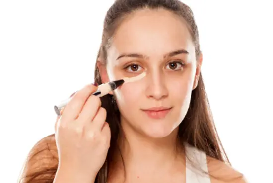 A young woman applying concealer under her right eyelid