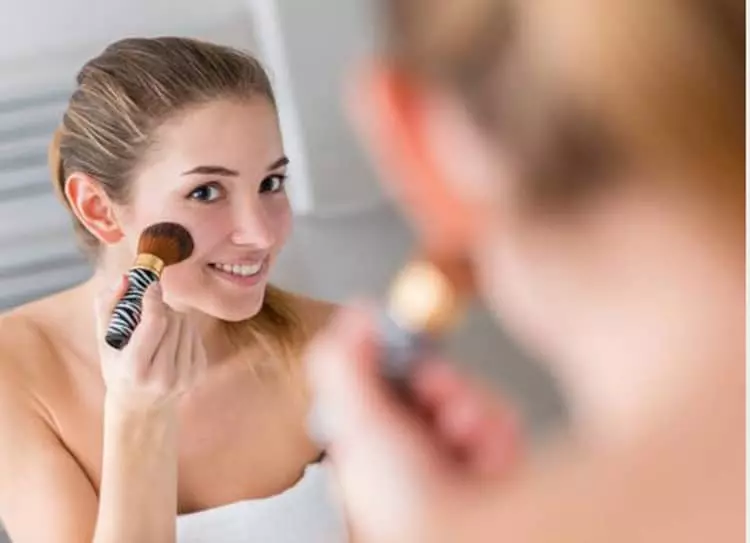 A happy young woman applying blush to her face