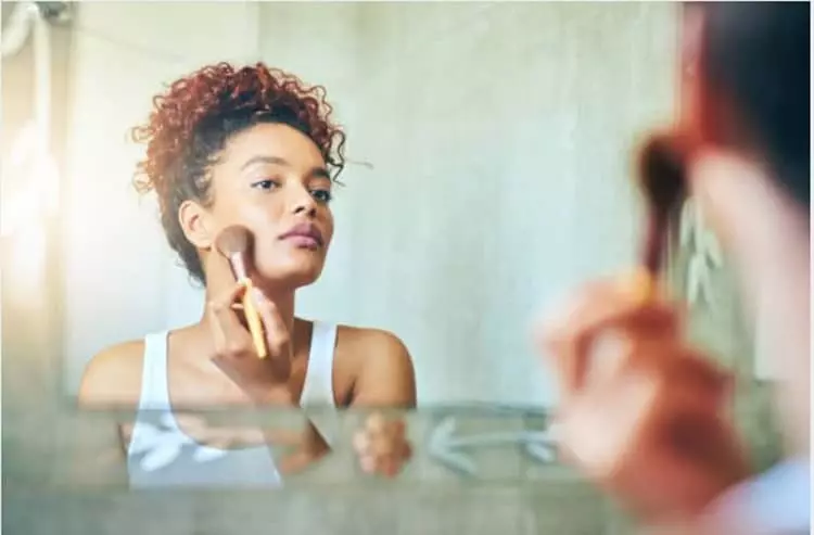 A woman using a brush to apply bronzer to her face