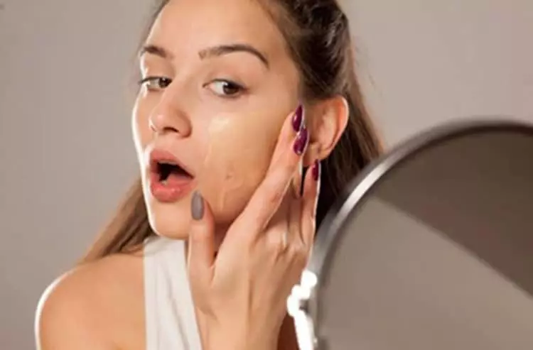 A pretty young woman using a portable mirror to apply foundation to her face