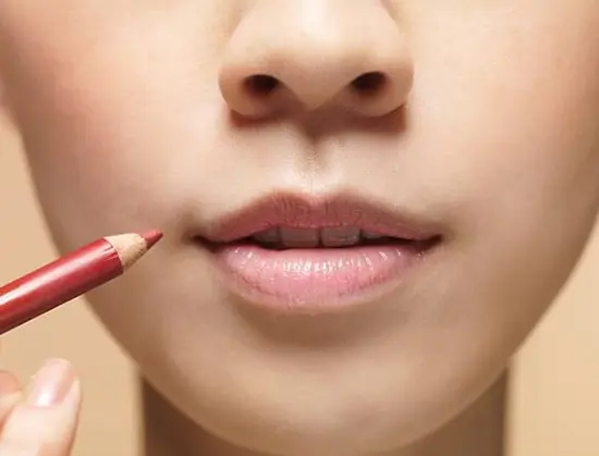 A young lady applying lip liner to her lips