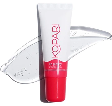 Close-up of a Kopari Coconut Lip Glossy in clear, featuring sleek packaging with a white and red design, placed against a textured background.