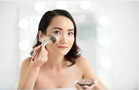 A lady applying highlighter to her face.