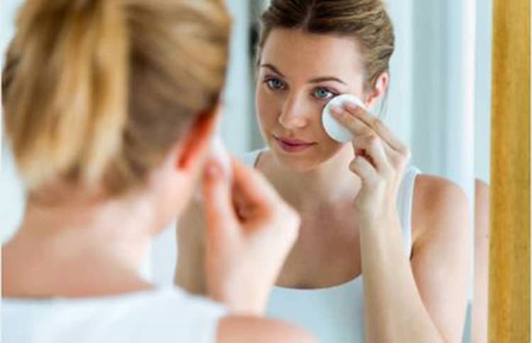 A young woman using a mirror to cleanse and moisturize her face