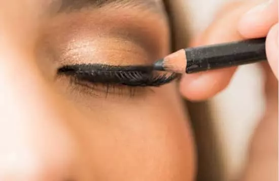 A woman precisely applies eyeliner to her eyelashes with a pencil, enhancing her eyes with a touch of elegance and definition