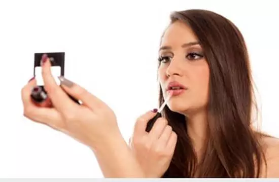 A young woman applying lipgloss to her lower lip while looking in the mirror