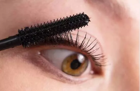 A closeup of a woman applying mascara to the base of the upper lashes of her eye with a wand