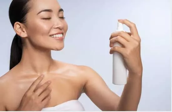 A pretty asian woman with a smile applying setting spray to her face