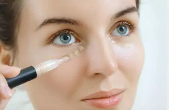 A young lady applying concealer under her right eyelid with a pen