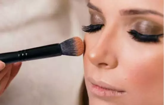 A young lady applying highlighter to her face with a highlighter brush.