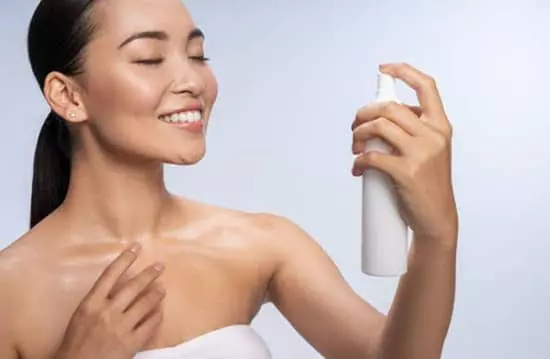 A young woman applying setting spray over her face